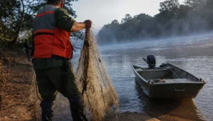 Agente de fiscalizacao recolhe rede na beira do rio, cena ligada a pescar em local proibido sem tirar o peixe da agua