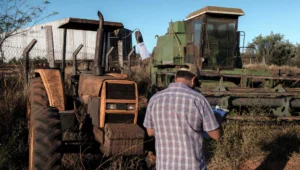 Trator e colheitadeira penhorados parados em pátio de depósito judicial, com homem de costas anotando os lotes em prancheta