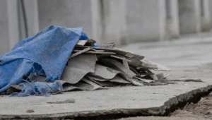 Telhas quebradas e lona azul rasgada sobre piso de concreto rachado, obra de contrapartida de TAC ambiental anos depois